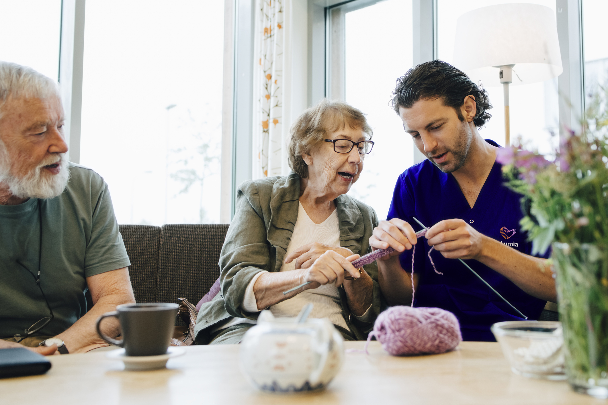 Senior woman teaching male nurse to knit